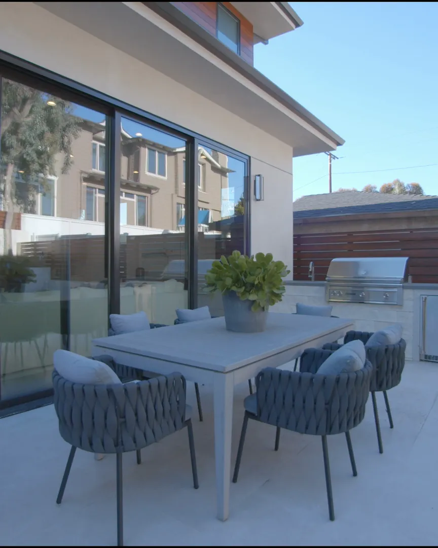 Terrasse mit Esstisch und Sitzgruppe vor großen Glasflächen, Gegenlicht