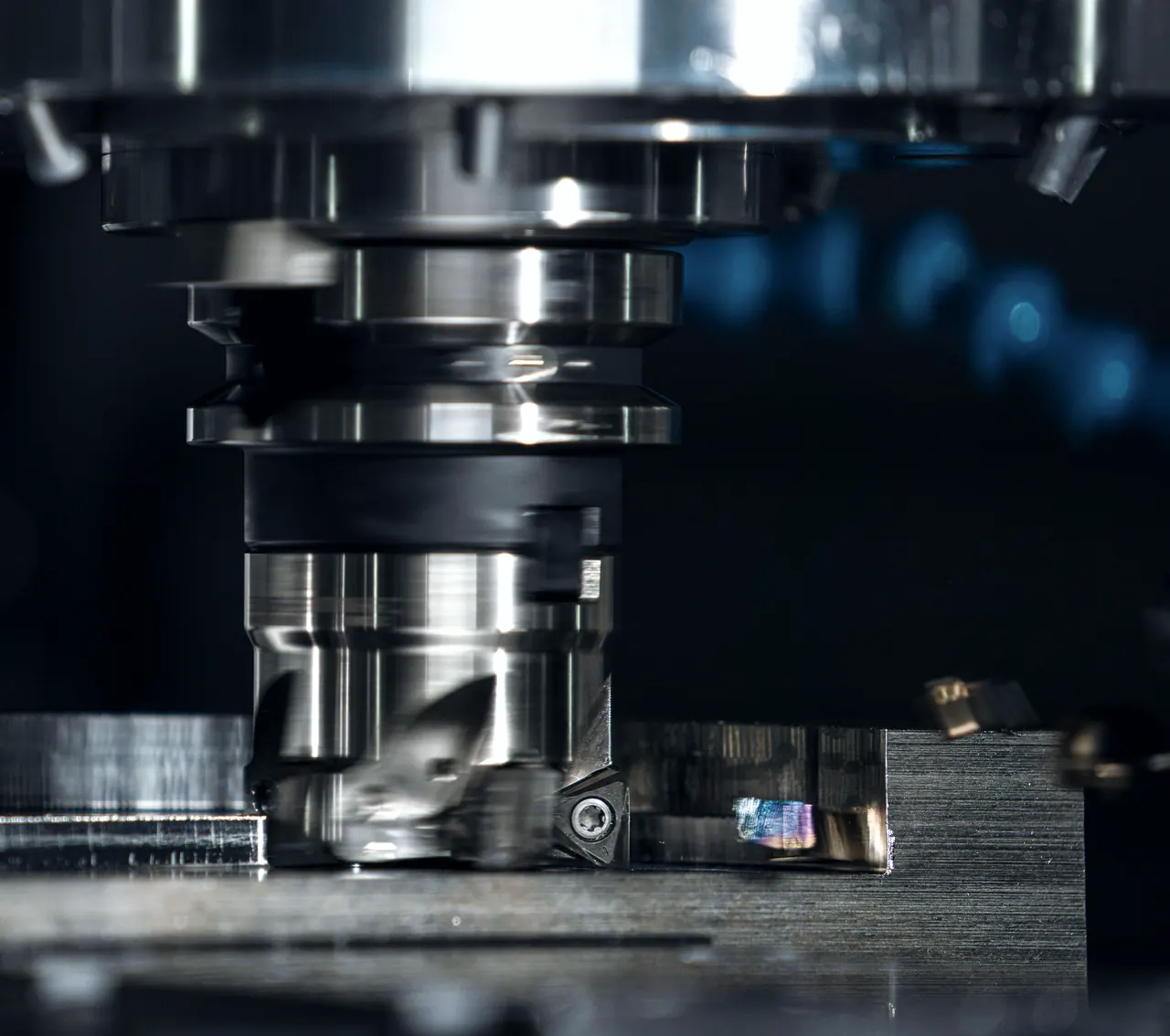 Nahaufnahme eines Messerkopfes an der Frässpindel über einem Metallblock, Kühlmittel blau unscharf im Hintergrund