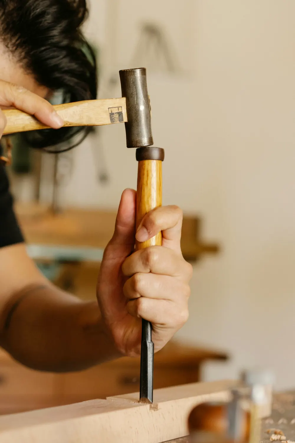 Hand mit Hammer und Stechbeitel an einem Holzbrett vor hellem Hintergrund